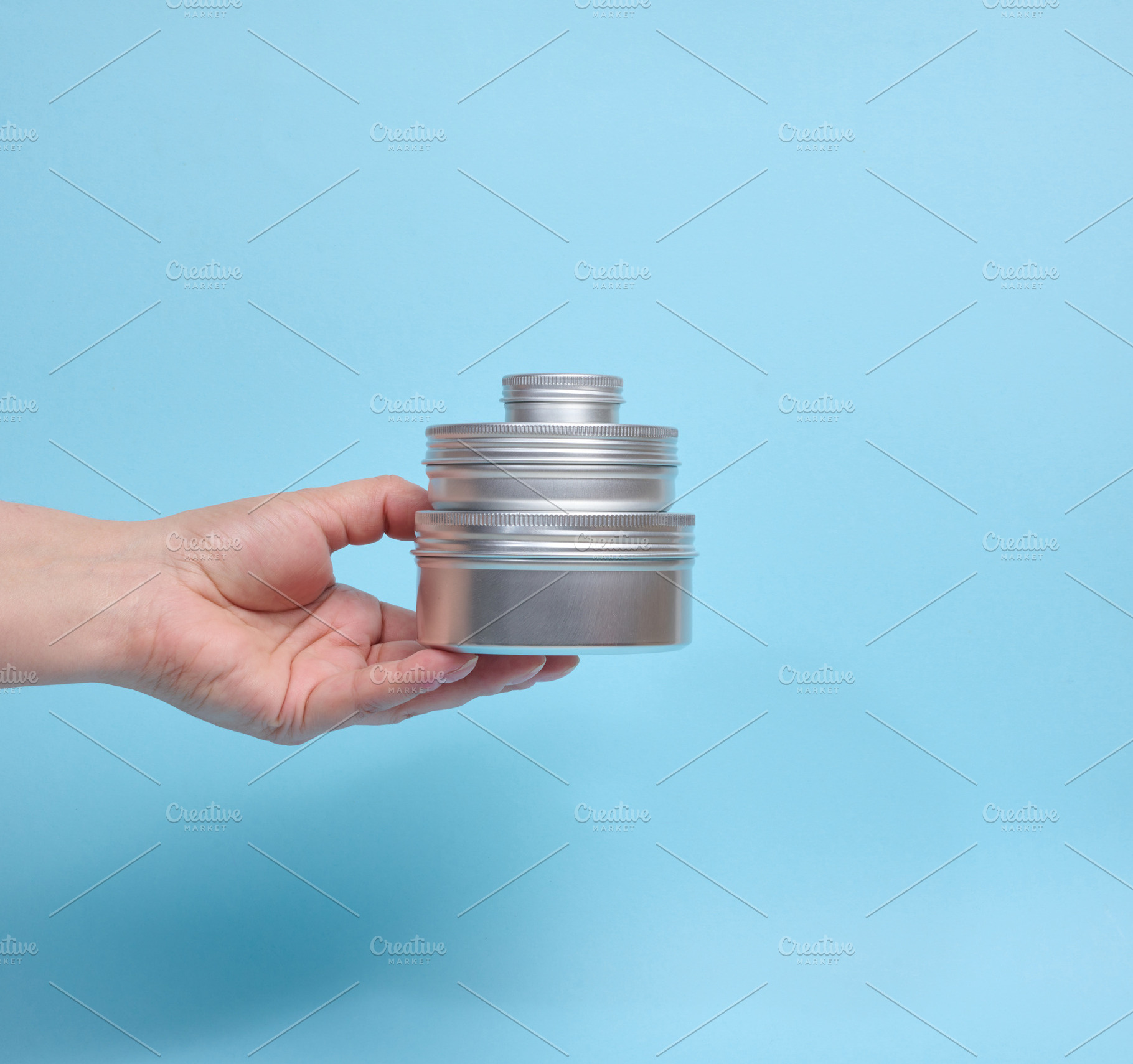 A person holding a pyramid of three round aluminum jars on their, a Beauty & Fashion Photo by ndanko