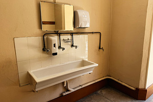 Vintage communal sink and soap dispensers in a tiled restroom corner in Paris,, a Photo by AS photostudio