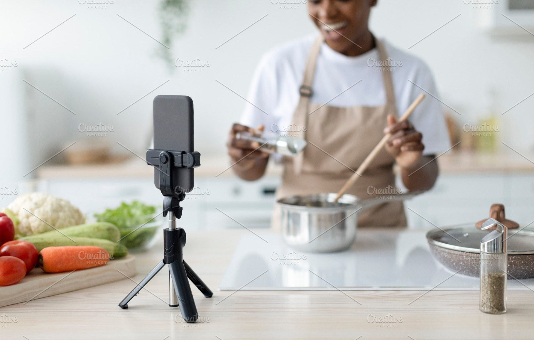 Satisfied millennial black lady in apron cooking at home shooting video lesson, a Person Photo by Prostock-Studio