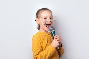 Cheerful young girl in yellow hoodie and playful glasses singing, a Person Photo by Ales Munt