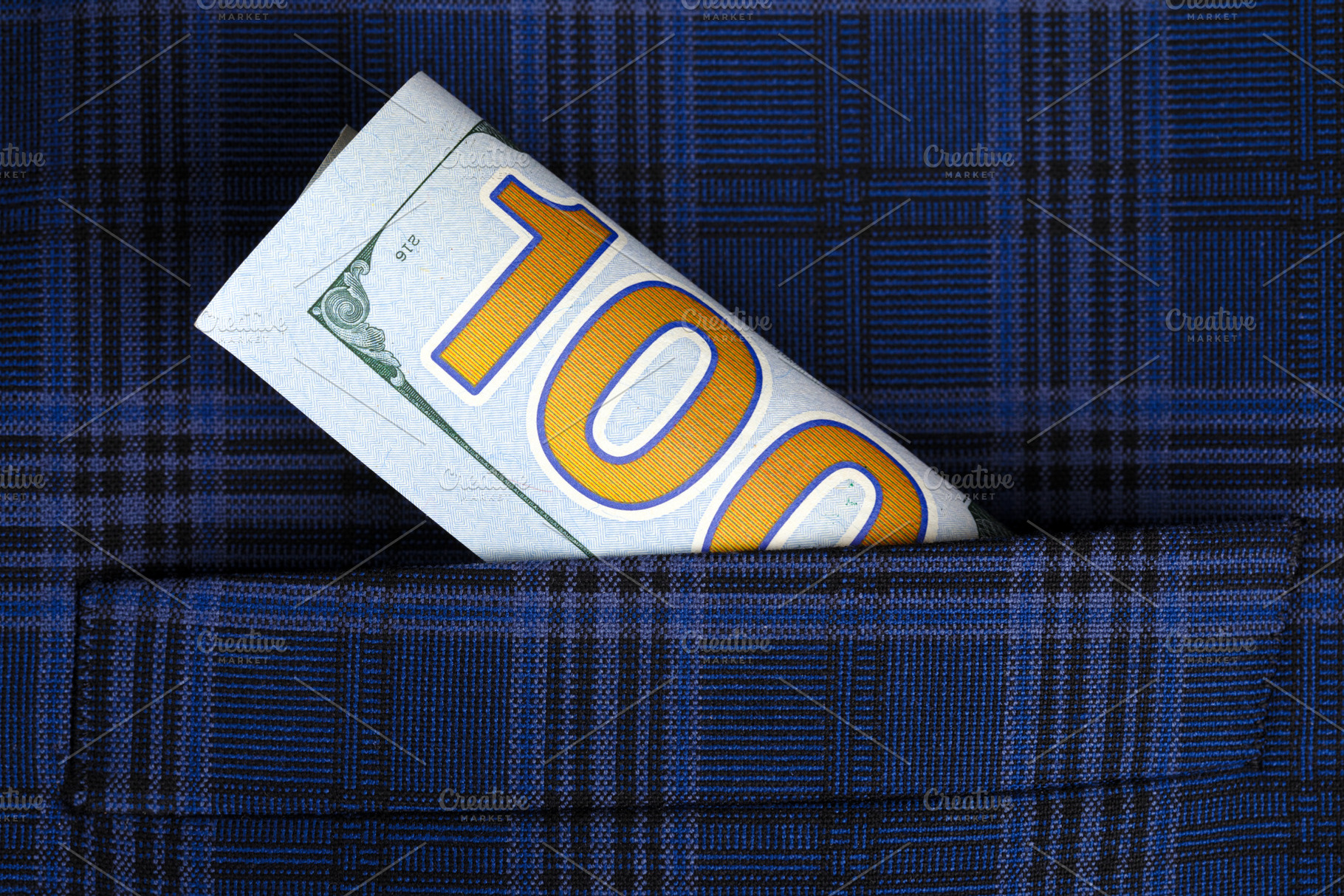 Rolled hundred dollar bill sticking out of a dark blue plaid fabric pocket, sym, a Business Photo by Ales Munt