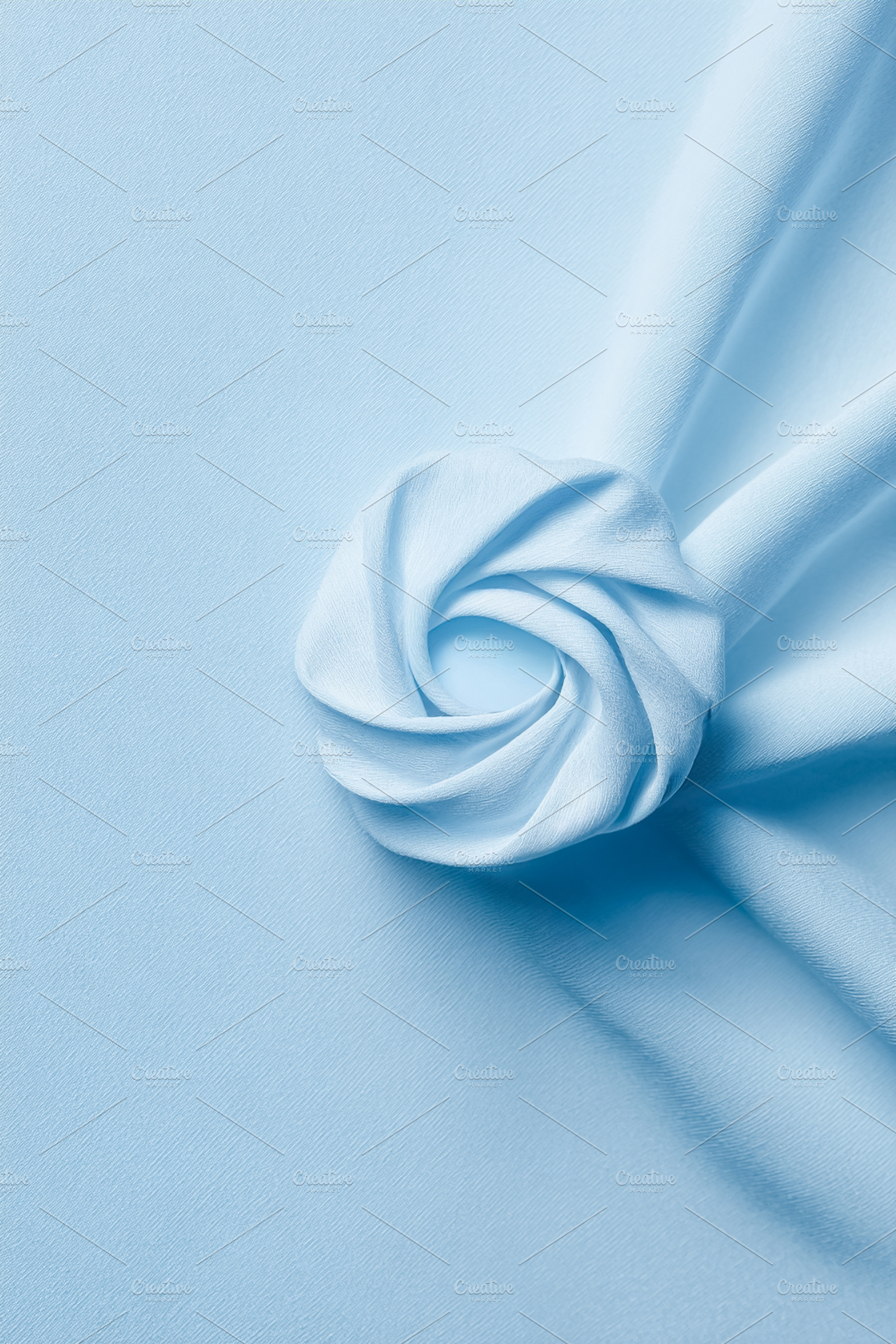Pastel blue fabric swirling creating a delicate rosette shape an, a Photo by Studio ANNA