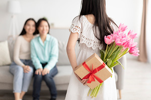 Women's Day celebration. Asian girl hiding gift and flowers behind back, congra, a Photo by Prostock-Studio