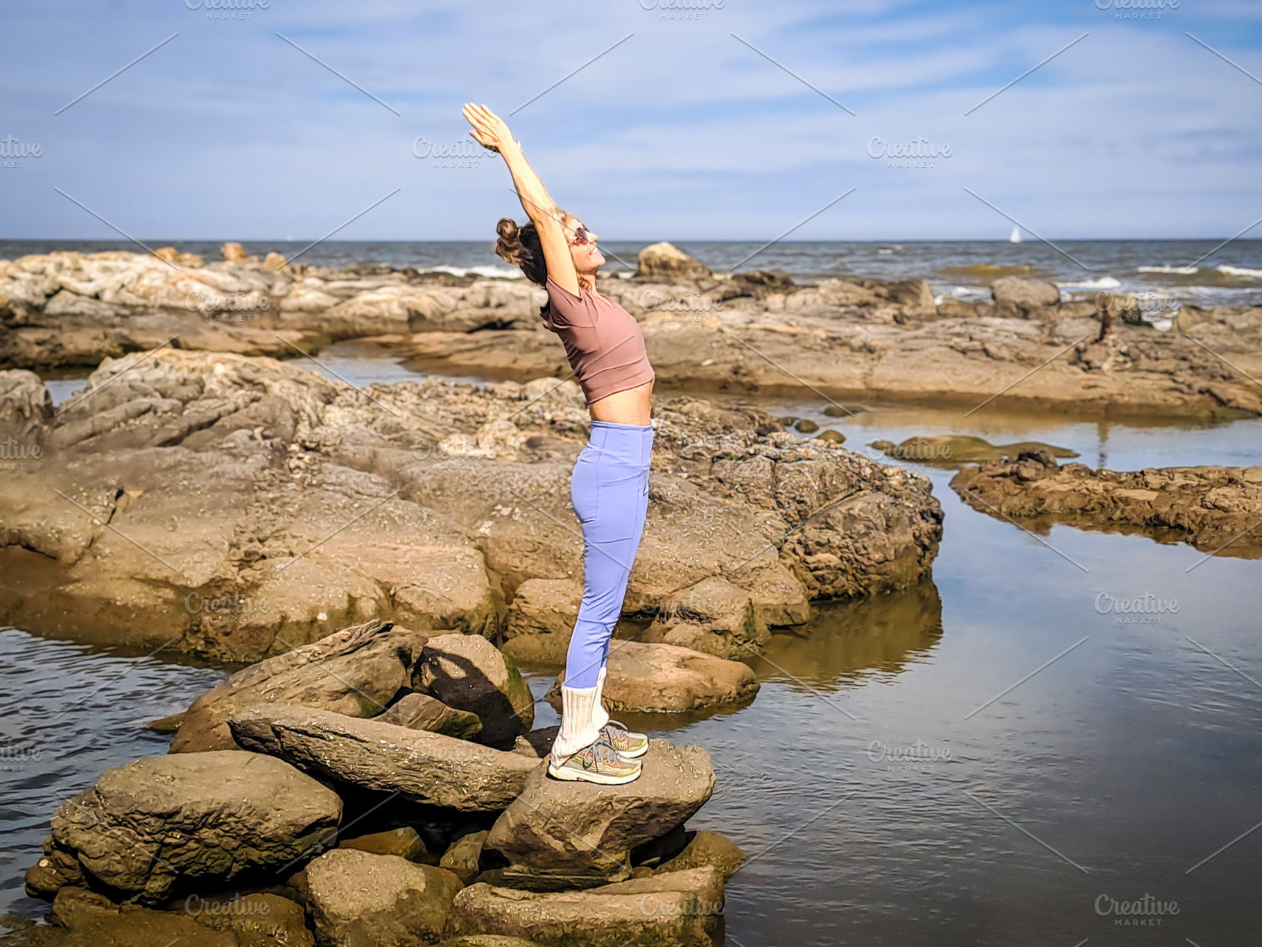 Woman stands on rocky coast holding a yoga pose with arms raised, a Health & Medical Photo by DanFLCreativo