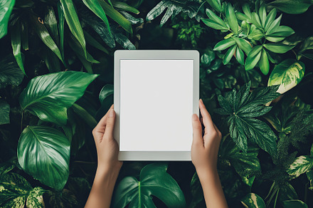 Holding a tablet among lush green foliage in a serene setting, a Technology Photo by AlyaAnd