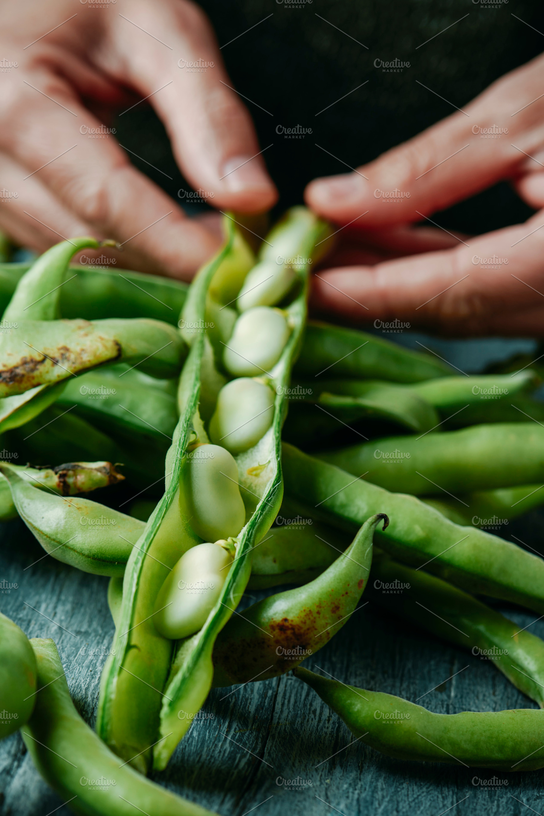closeup of a man taking broad beans out of its pod, a Photo by Nito