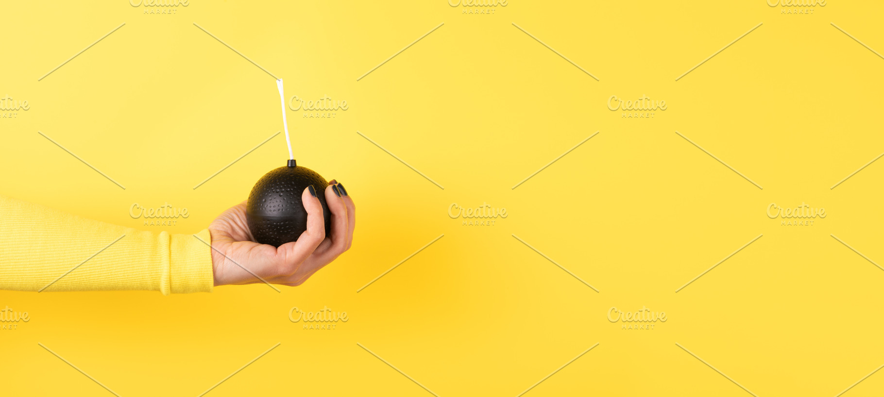 A female hand in a yellow sleeve holds a round black cartoon bom, a Person Photo by Ales Munt