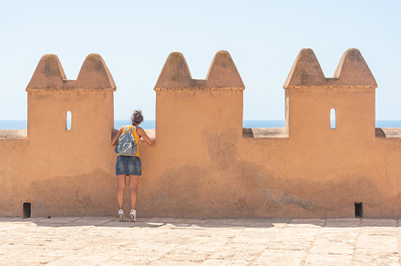 Anonymous female traveler near aged towers near sea, a Holiday Photo by Iván Moreno STOCK PHOTO