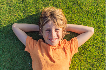 Boy lying on green grass looking at, a Nature Photo by Elizaveta Galitskaya