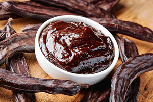 carob cream in a bowl among pods on a wooden table, a Photo by Nito