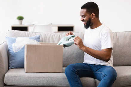 Smiling African Customer Guy Unpacking Box With New Clothes Indoor, a Background Photo by Prostock-Studio