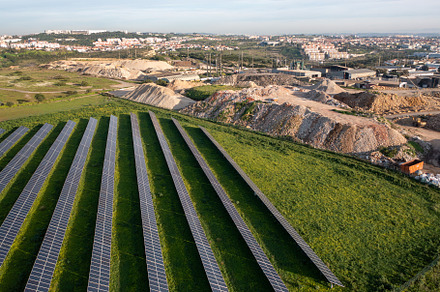 Solar panels dot an expansive green landscape near a construction site on a cle
