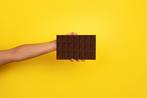 Close-up of an extended hand holding a large dark chocolate bar, a Food & Drink Photo by Ales Munt