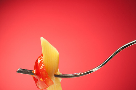 Fork with pasta and tomato on a red background