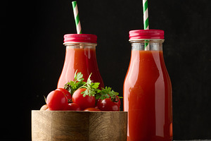 Glass bottles with tomato juice on black table and wooden bowl w, a Food & Drink Photo by ndanko
