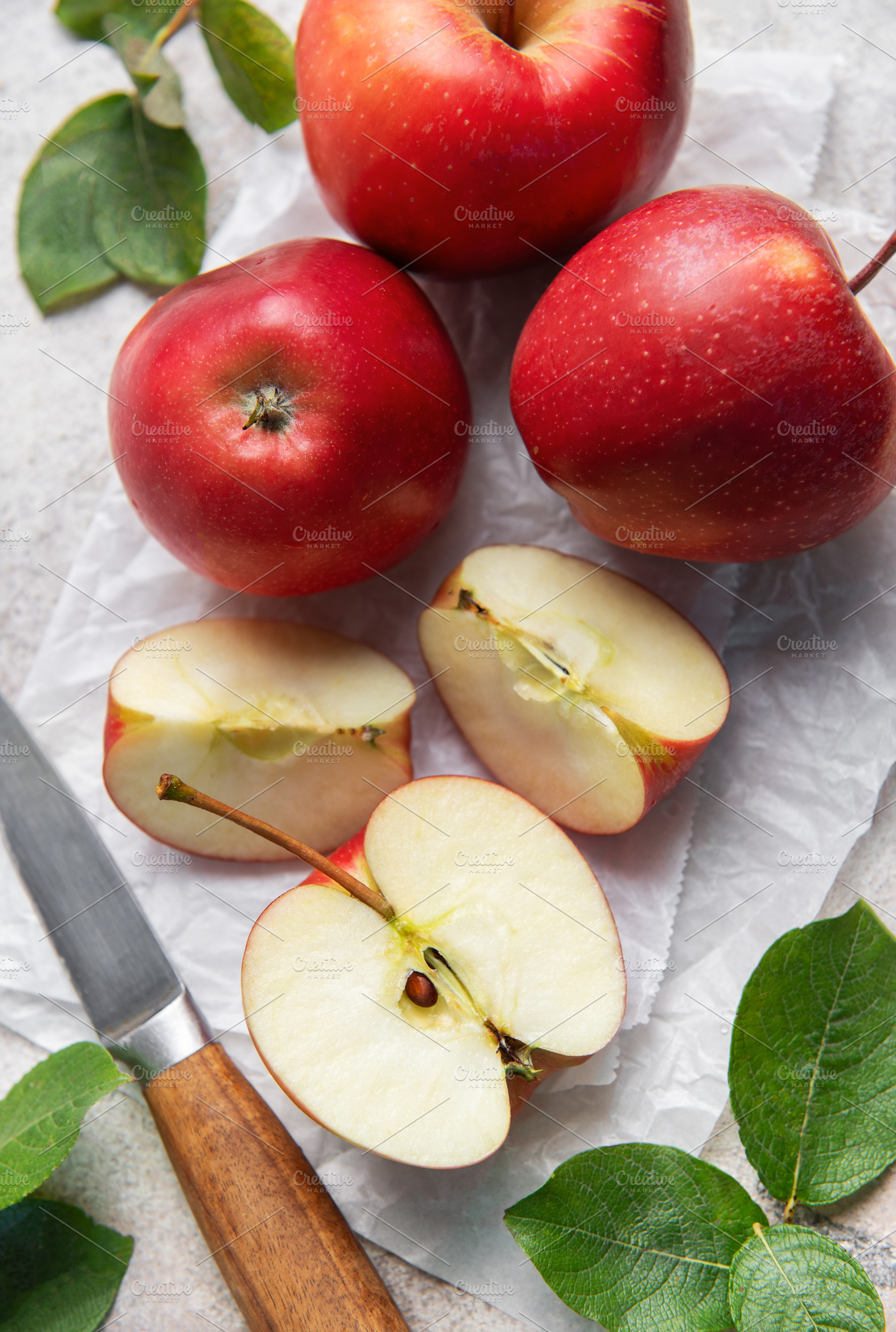 Freshly cut red apples on baking paper with knife and leaves, a Food & Drink Photo by Olena Rudo