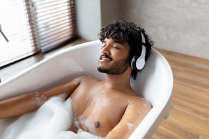 Relaxed indian man listening to calming music in wireless headphones, lying in, a Person Photo by Prostock-Studio