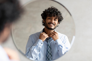 Excited indian businessman getting ready and buttoning up shirt, standing in ba, a Person Photo by Prostock-Studio
