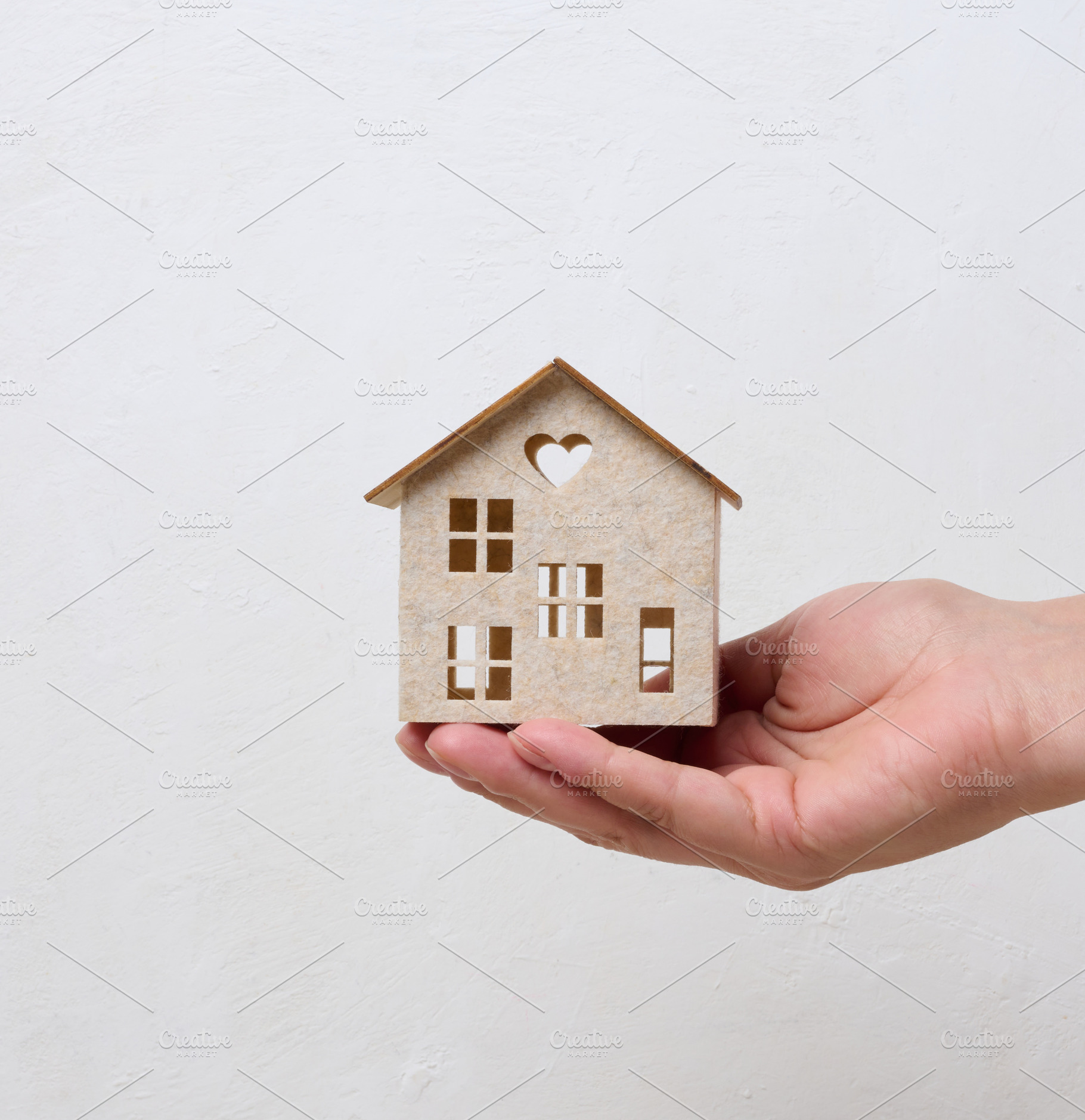 A person holding a small wooden house model on their palm agains, a Business Photo by ndanko