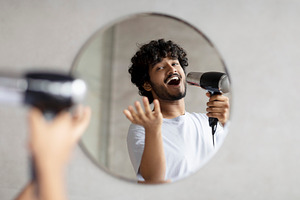 Playful indian guy holding hairdryer and singing as in microphone, doing mornin, a Photo by Prostock-Studio