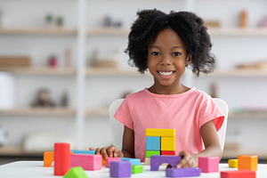 Portrait of cheerful adorable kid playing with wood blocks, a Photo by Prostock-Studio
