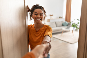 Cheerful African Woman Shaking Hands In Opened Door At Home, a Photo by Prostock-Studio