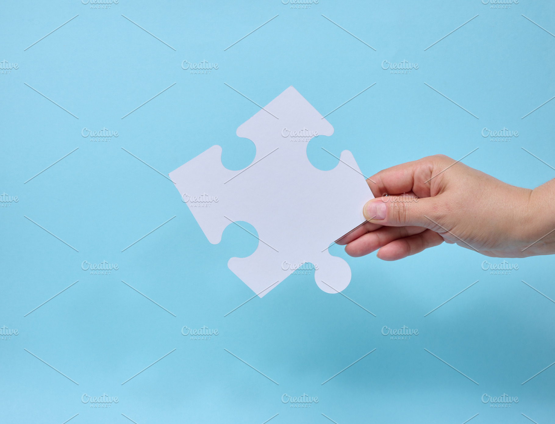 A person holding a single white puzzle piece against a blue back, a Business Photo by ndanko
