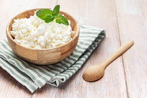 Cottage cheese in wooden bowl with mint on rustic table, a Food & Drink Photo by Olena Rudo