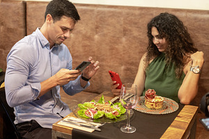 Young couple using smartphones while waiting for food at restaurant, a Person Photo by etorres69