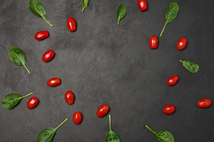 Scattered spinach leaves and red cherry tomatoes on black backgr, a Food & Drink Photo by ndanko