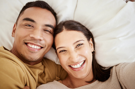 Happy, smiling and in love young couple enjoying spending time together at home in bed inside. Portrait of romantic and loving partners with a smile looking cheerful, positive and excited for the day, a Photo by Peopleimages.com
