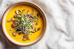 A bowl of rich pumpkin soup placed on a linen napkin, topped with seeds and fre, a Food & Drink Photo by AlyaAnd