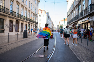 Woman with rainbow flag around her walking on tramway at city street, a Person Photo by andreonegin market