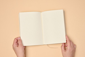 Hands hold a blank open notebook on a neutral background, an Abstract Photo by ndanko