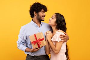 Celebration concept. Loving indian couple embracing and man holding wrapped gif, a Photo by Prostock-Studio