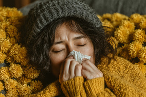 Woman blowing nose surrounded by yellow flowers, feeling unwell during winter, a Health & Medical Photo by AS photostudio
