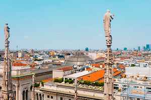 statues of the Duomo looking over Milan skyline, a Photo by Nito