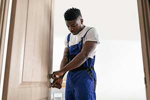 African American Repairman Fixing Door Standing Indoor, Wearing Coverall, a Photo by Prostock-Studio