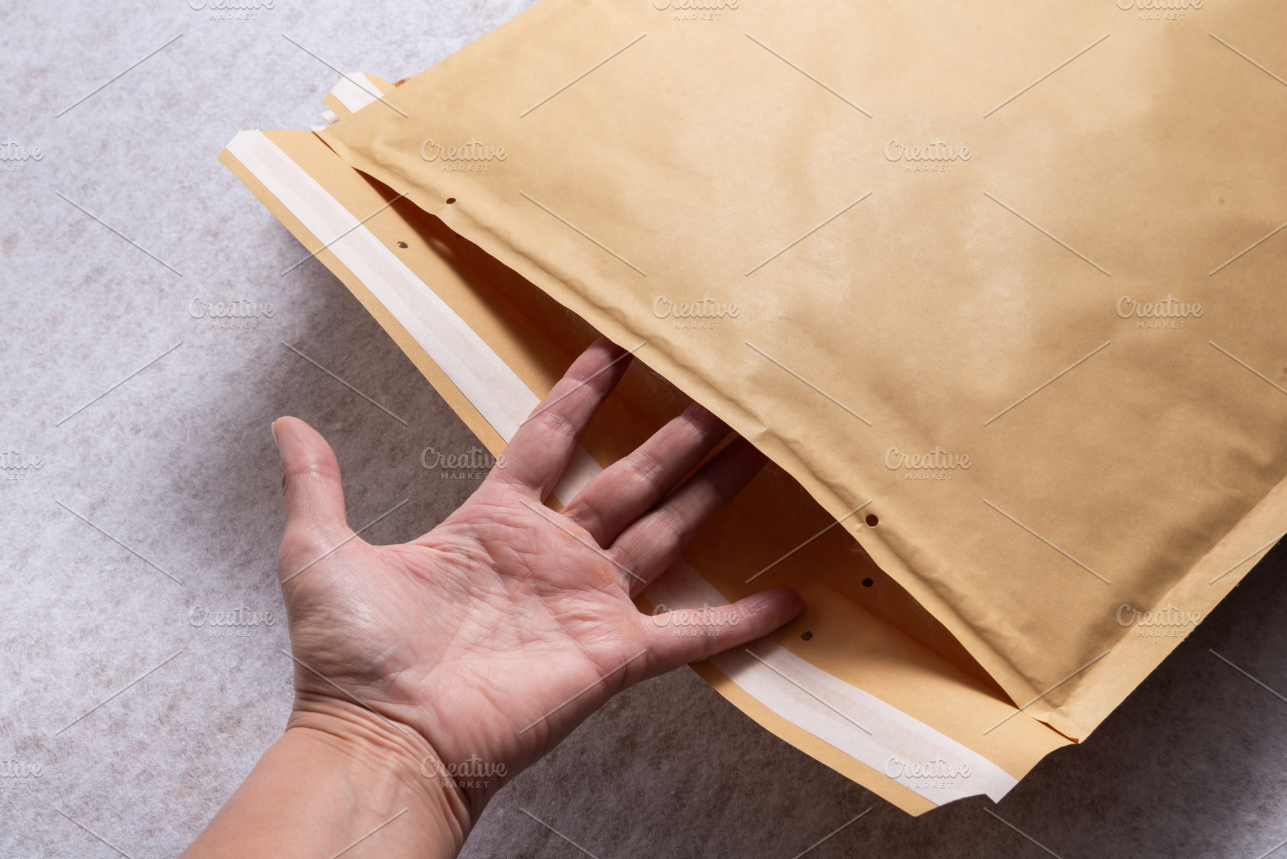 Female Hand Opening Bubble Mailer Plastic Padded Envelope on Whi, an Industrial Photo by MDBildes
