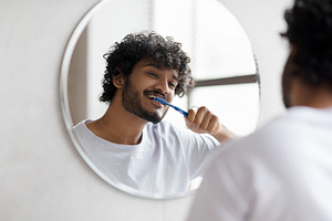 Dental care. Happy indian man brushing his teeth with toothbrush in bathroom, s, a Person Photo by Prostock-Studio