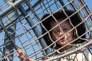 Young girl in a sun hat climbing a rope net structure against a clear blue sky,, a Person Photo by Ales Munt