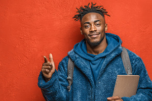 Confident young student holding a notebook in front of a vivid red wall, a Photo by AS photostudio