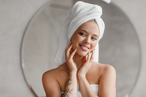 Self care day. Pretty lady wrapped in towels looking at mirror in bathroom, doi, a Photo by Prostock-Studio
