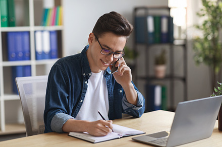 Young Office Manager Talking On Mobile Phone And Taking Notes To Notepad