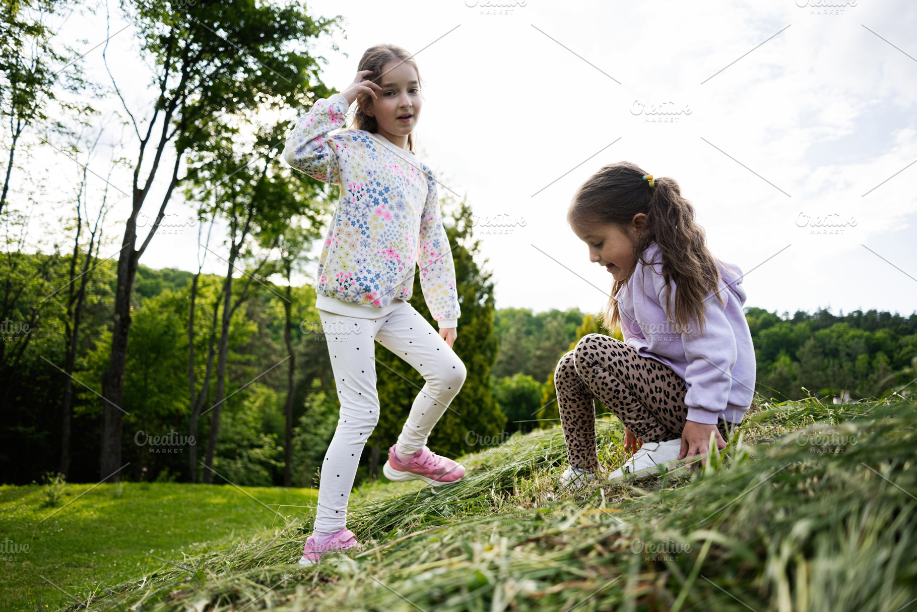 Two young girls enjoying a playful time in a lush green outdoor setting, a Person Photo by AS photostudio