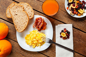Scrambled eggs with bacon, bread, orange juice and dried fruit composing a full, a Food & Drink Photo by Antonio Gravante Market