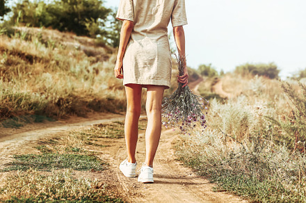 A girl with a bouquet of autumn flowers walks along an autumn road with her bac