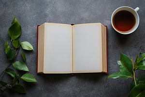 Open book with blank pages beside a cup of tea and green leaves on a gray surfa, a Background Photo by AlyaAnd