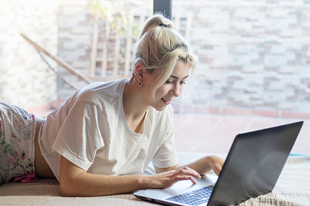 Photo of young joyful woman in pajama typing on laptop and smiling while lying, a Person Photo by 2Design
