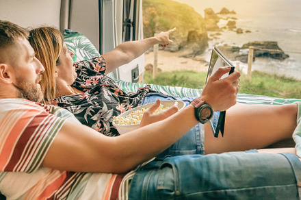 Couple watching a movie on the tablet eating popcorn lying on the bed of their, a Holiday Photo by davidpereiras